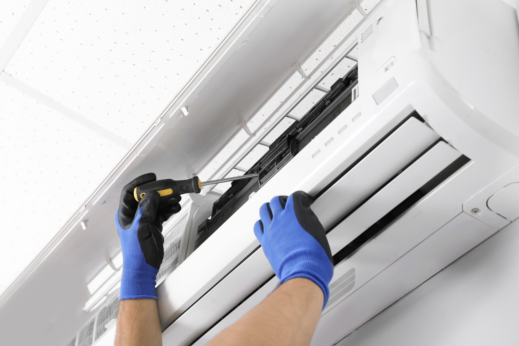 Blue-gloved hands servicing indoor air-conditioning equipment