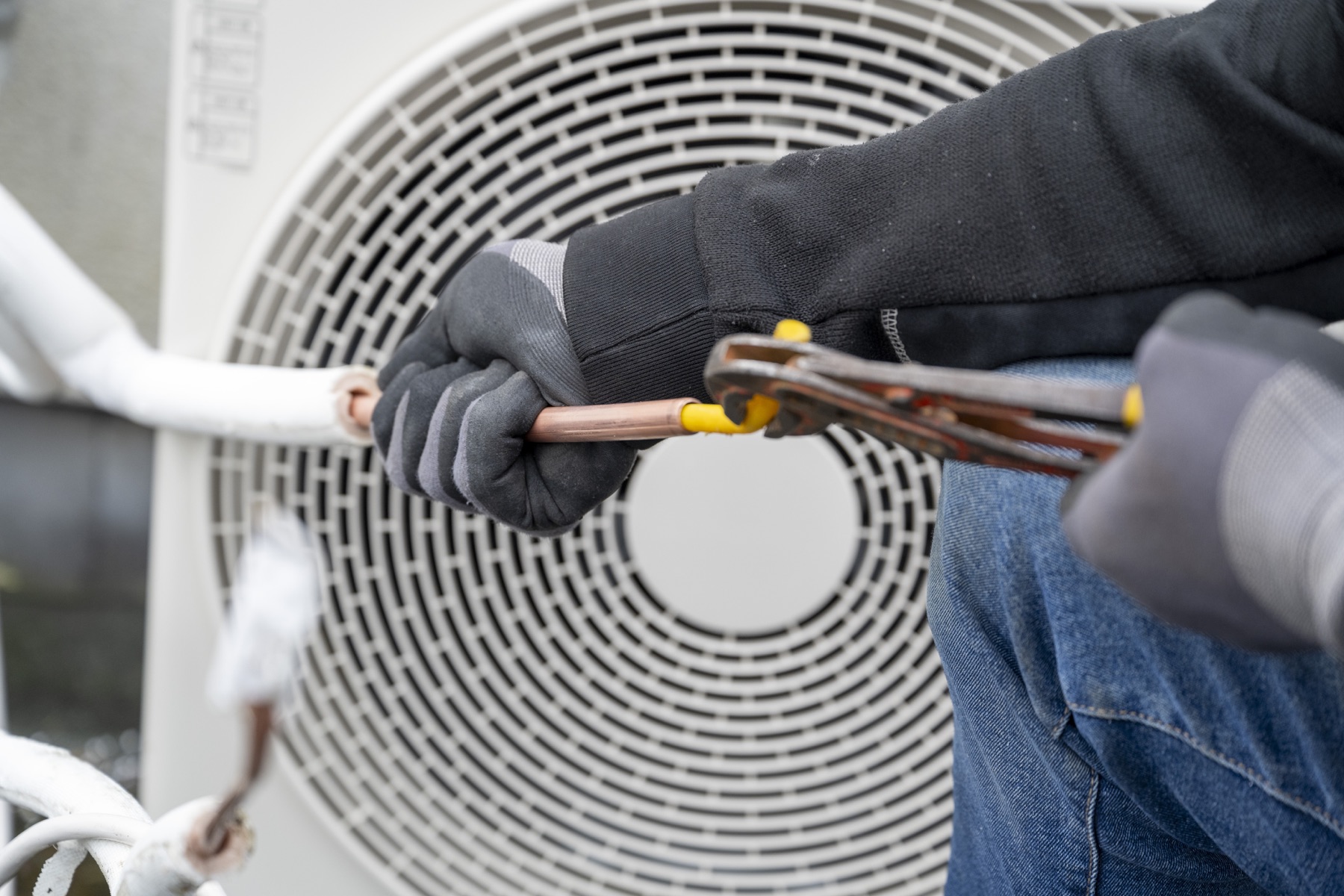 Gloved hands using pliers on air-conditioning equipment