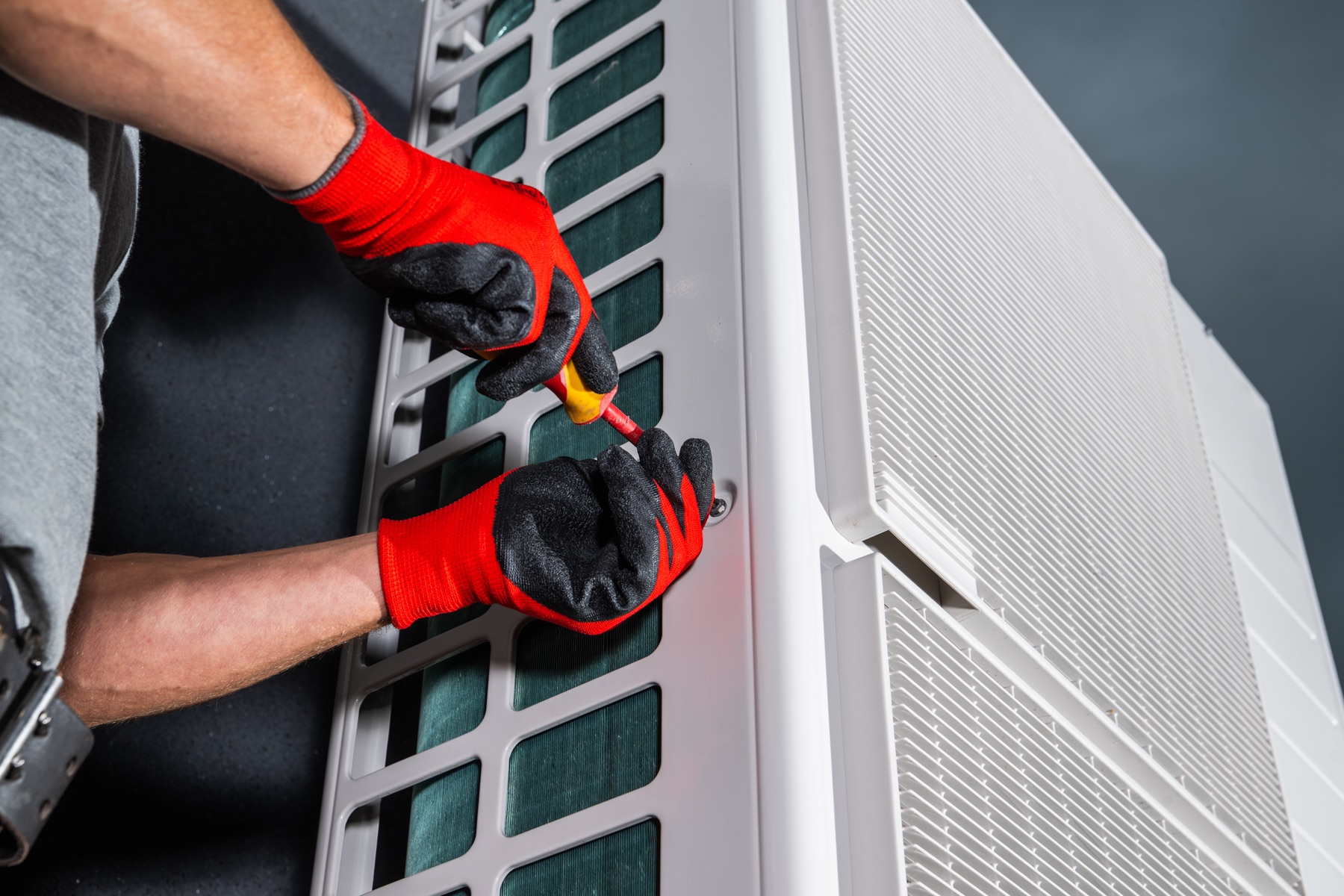 Gloved hands servicing an outdoor air-conditioning unit