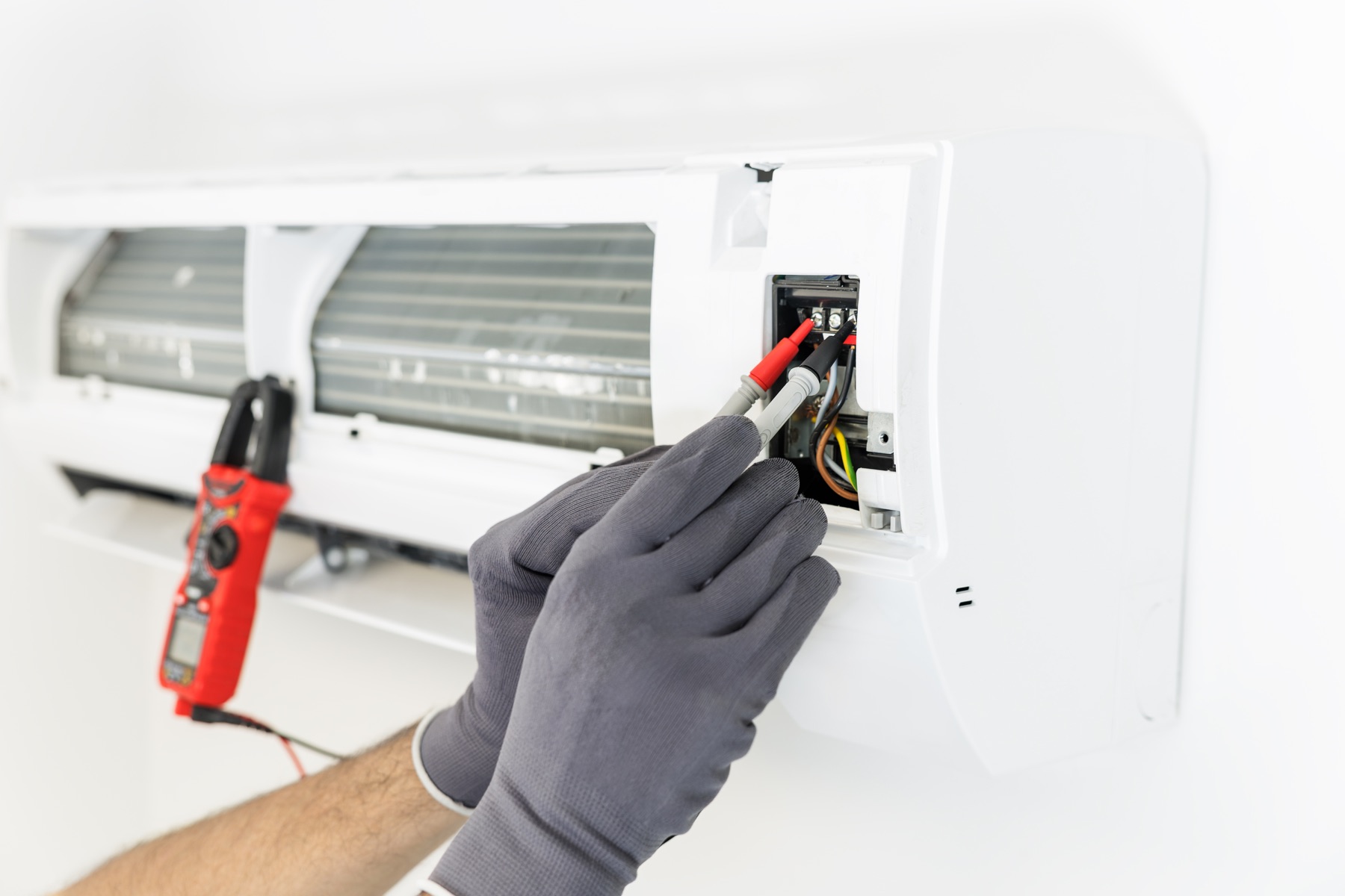 Gloved hands using a multimeter to test cooling equipment