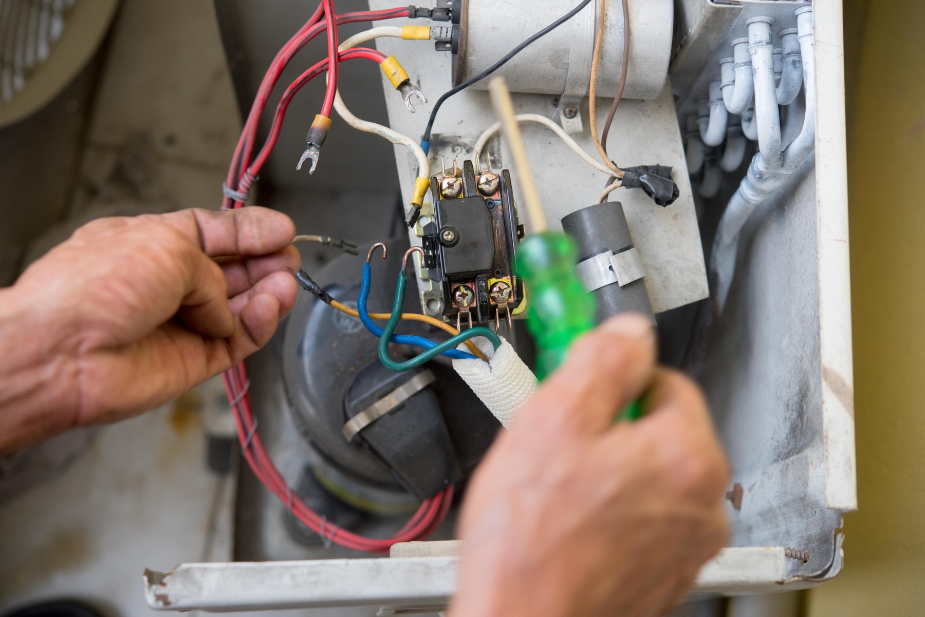 Hands inspecting electrical wiring in HVAC equipment